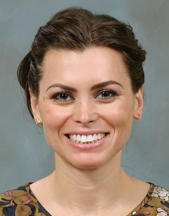 Smiling woman with braided brown hair wearing a patterned top against a gray backdrop